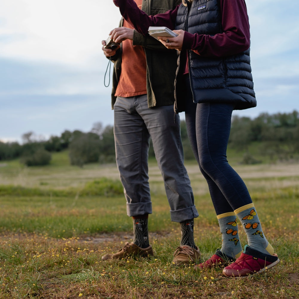 A couple out birding, holding a notebook and camera, wearing Darn Tough bird socks