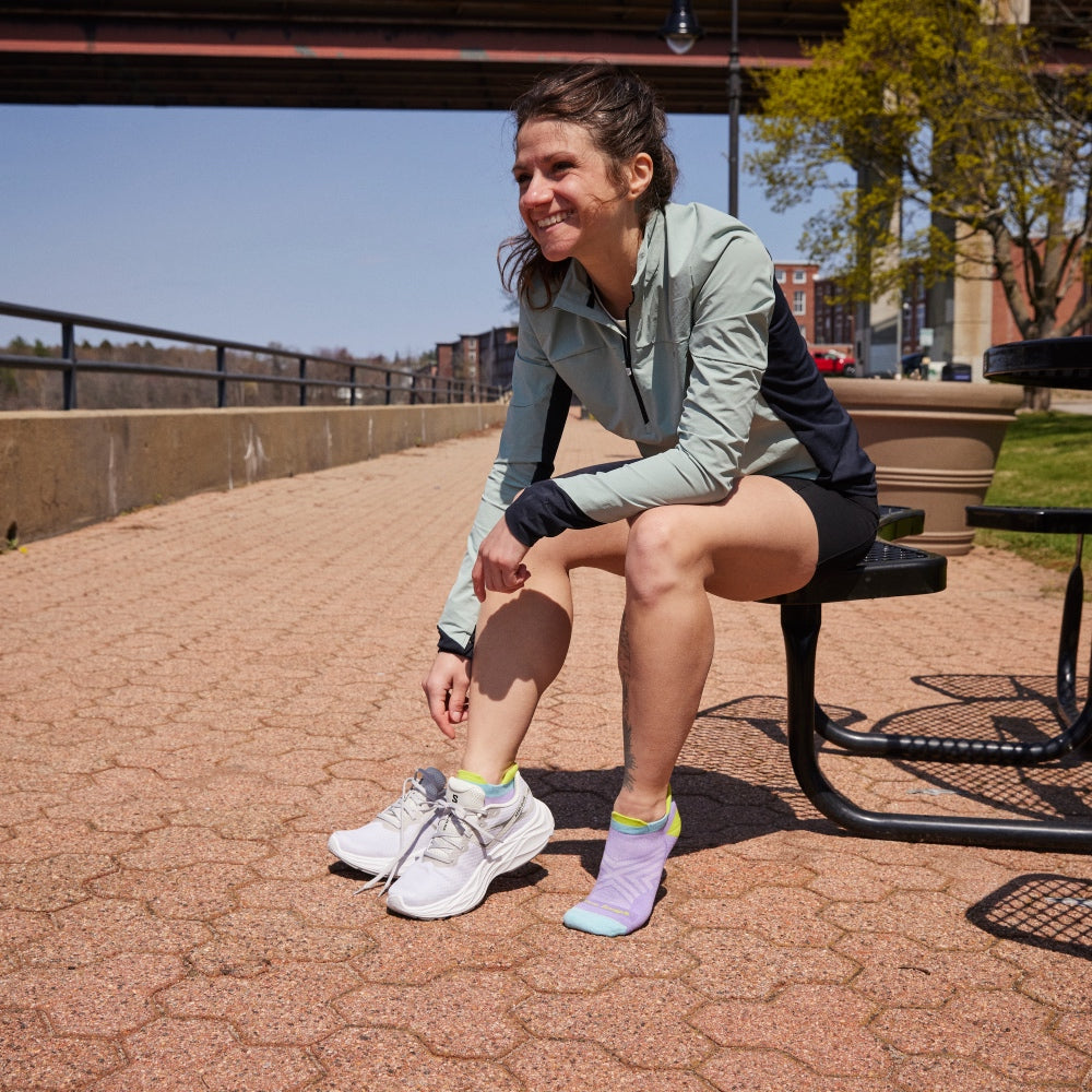 A lady runner seated on a bench adjusting her shoes and showing off the best women's running socks