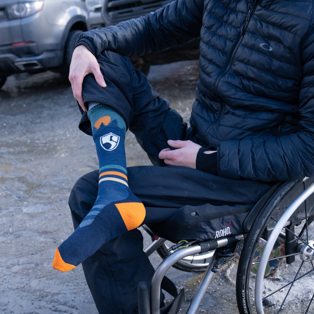 A person seated in a wheelchair wearing the High Fives sock from Darn Tough