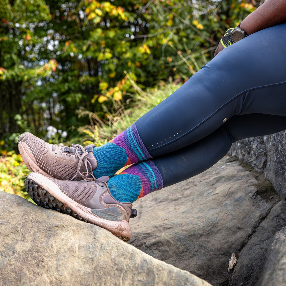 Runner Mirna Valerio seated on a rock showing off her feet in her Mirnavated running sock by Darn Tough