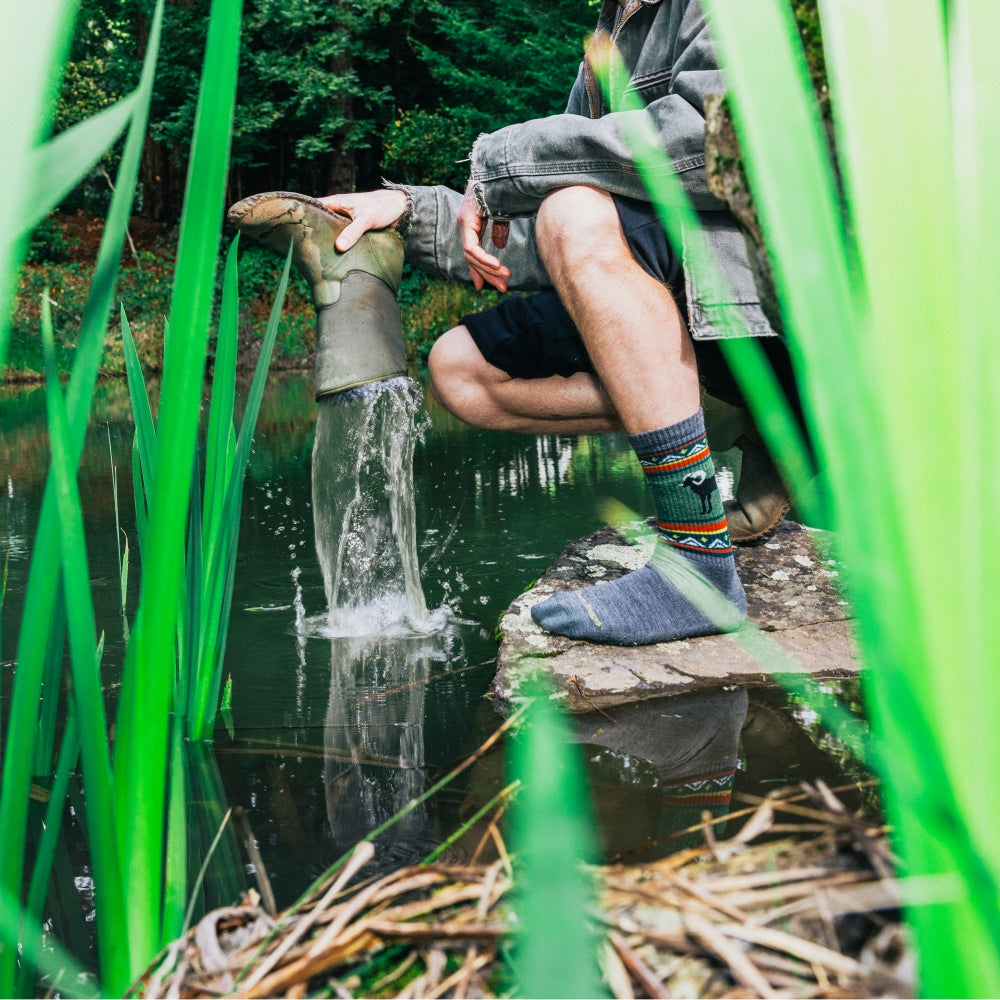 A person pouring water out of their rubber boot, wearing merino wool socks