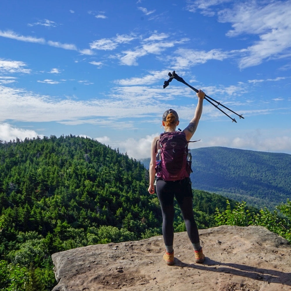 Alex standing on the summit of a mountain in NYC, holding her hiking poles above her head