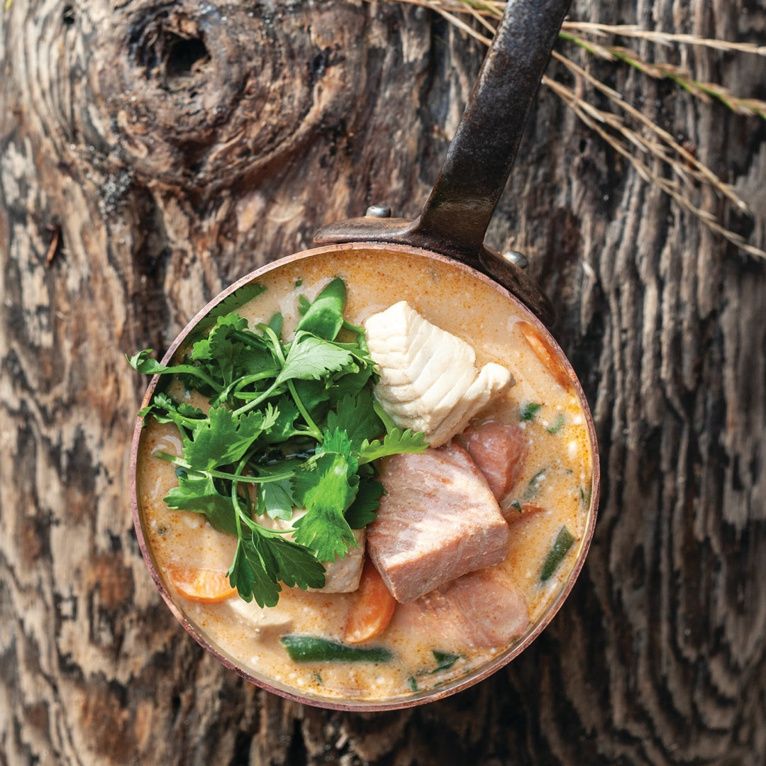 A bowl full of coconut curry soup, a creamy soup with salmon chunks, garnished with cilantro