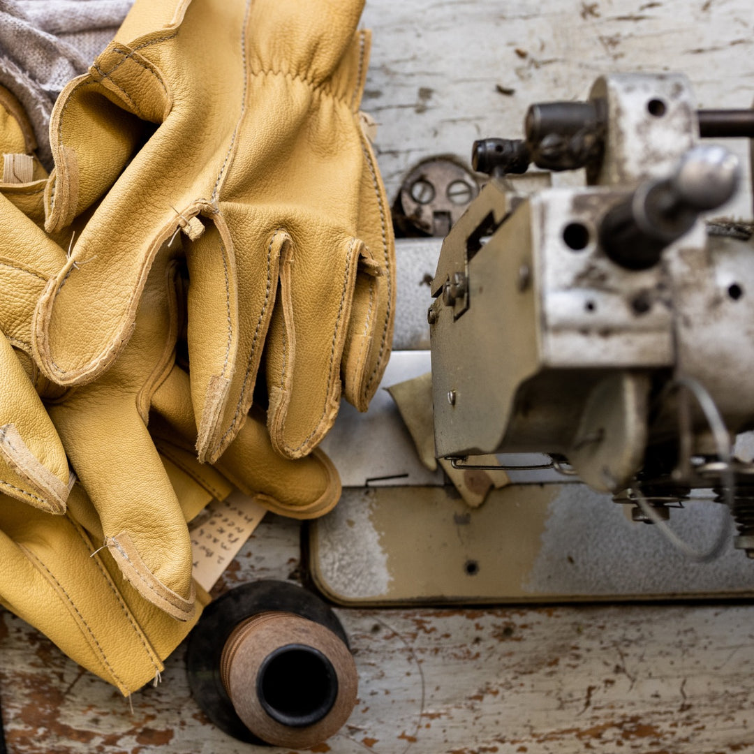 A pair of Vermont Glove leather work gloves next to a sewing machine