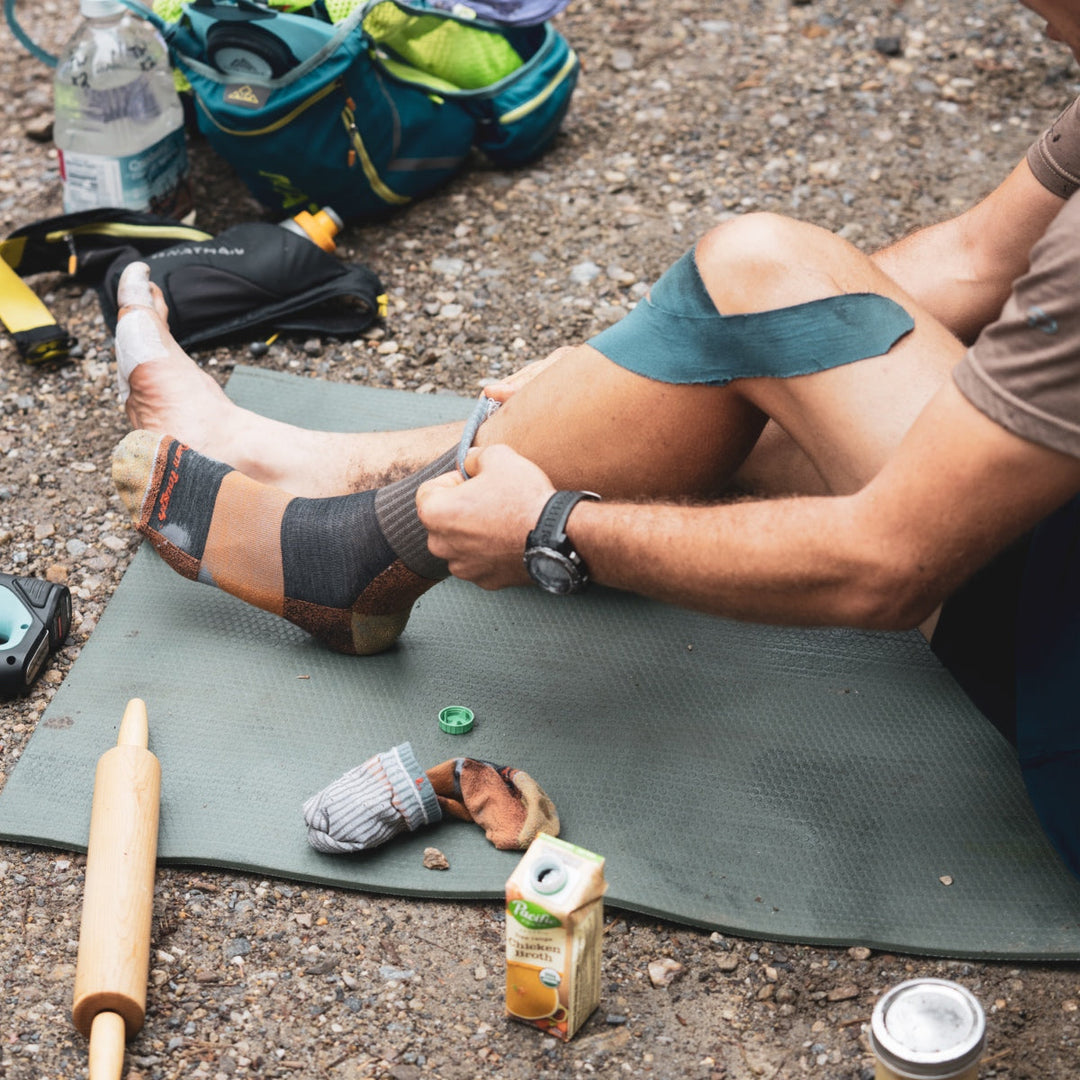 Ultrarunner seated pulling on well-worn darn tough socks, the most durable socks