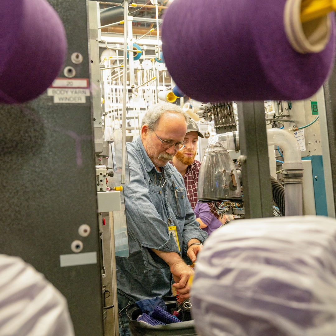 A Darn Tough employee showing another employee how to fix the knitting machine