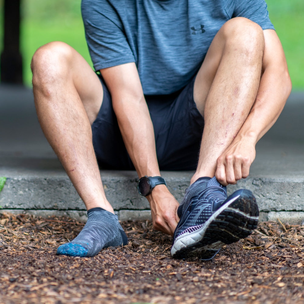 Person seated ground wearing no show running socks and putting on running shoes
