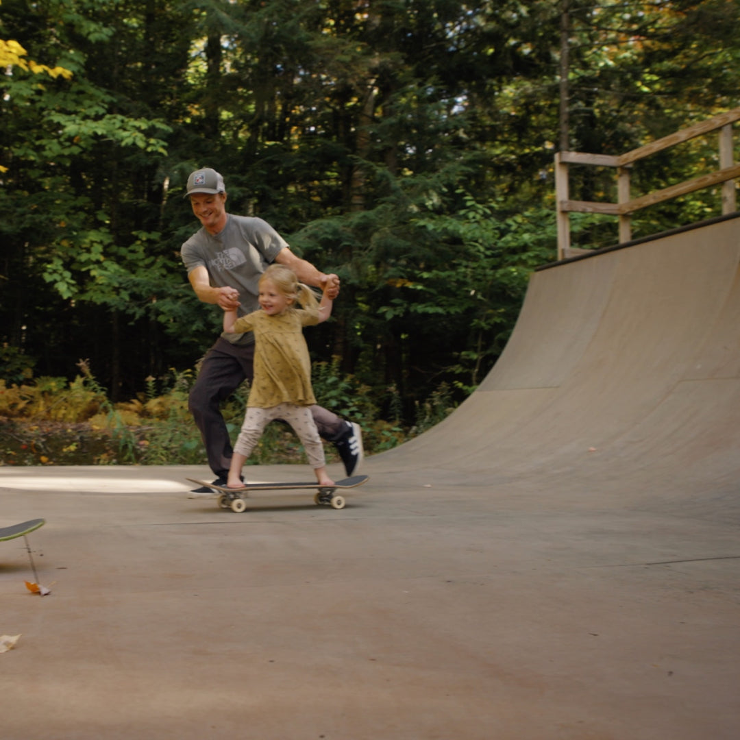 Jake Blauvelt holds his daughter's hands as she rides a skateboard down the ramp