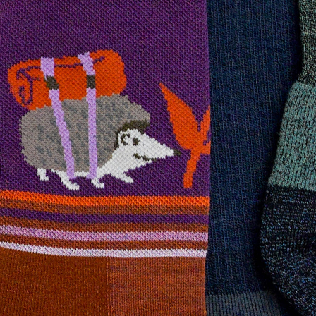 An adorable animal sock with a backpacking hedgehog next to some other hiking socks