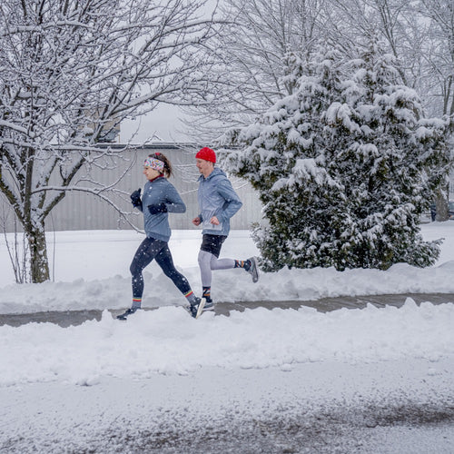 Two runners outside running in the winter, with snow falling around them