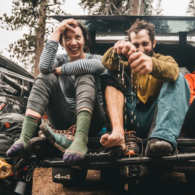 Three hikers on rainy day wearing moisture wicking socks, seated on tailgate drying off
