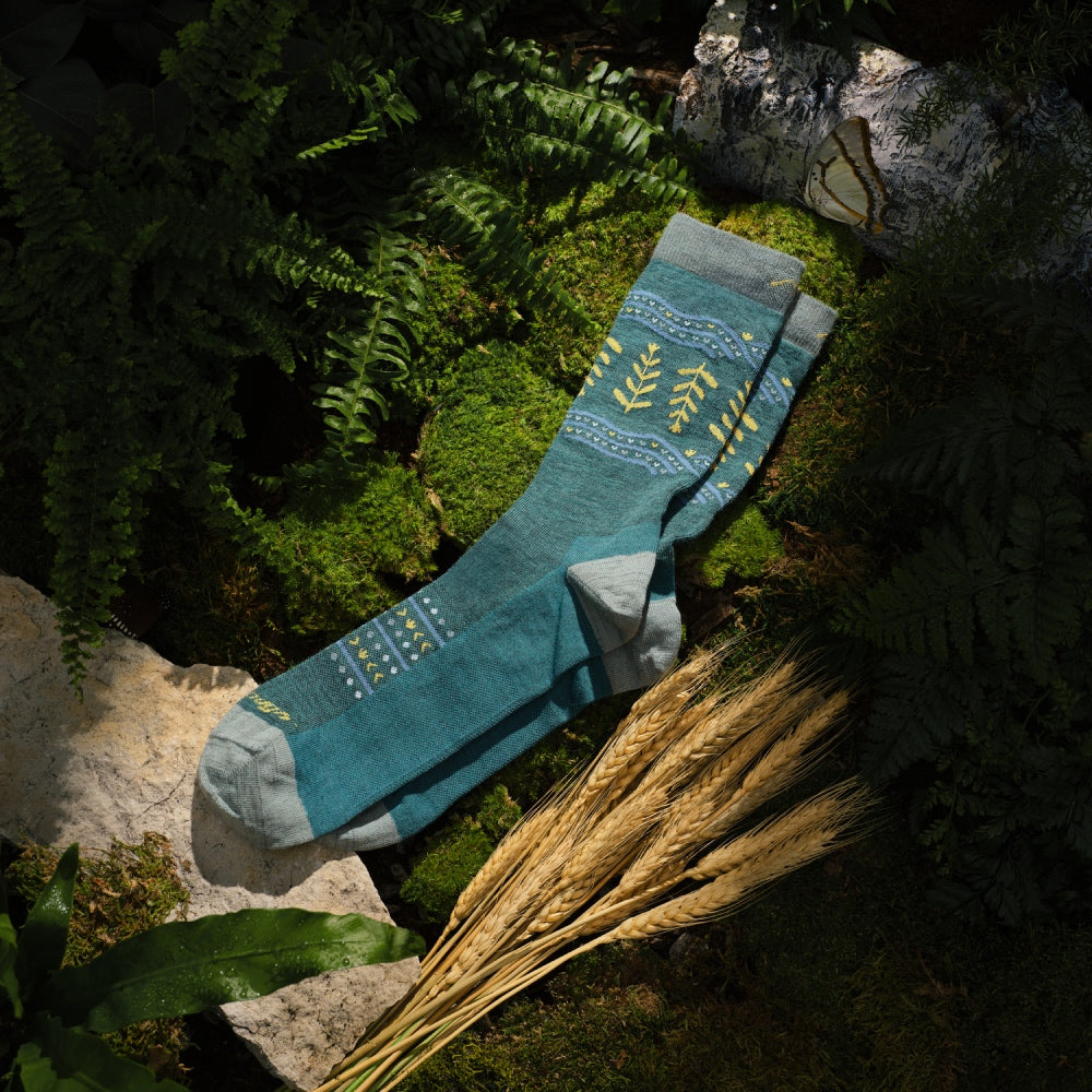 A pair of Grain or Shine socks laid out on some moss next to a bundle of grain
