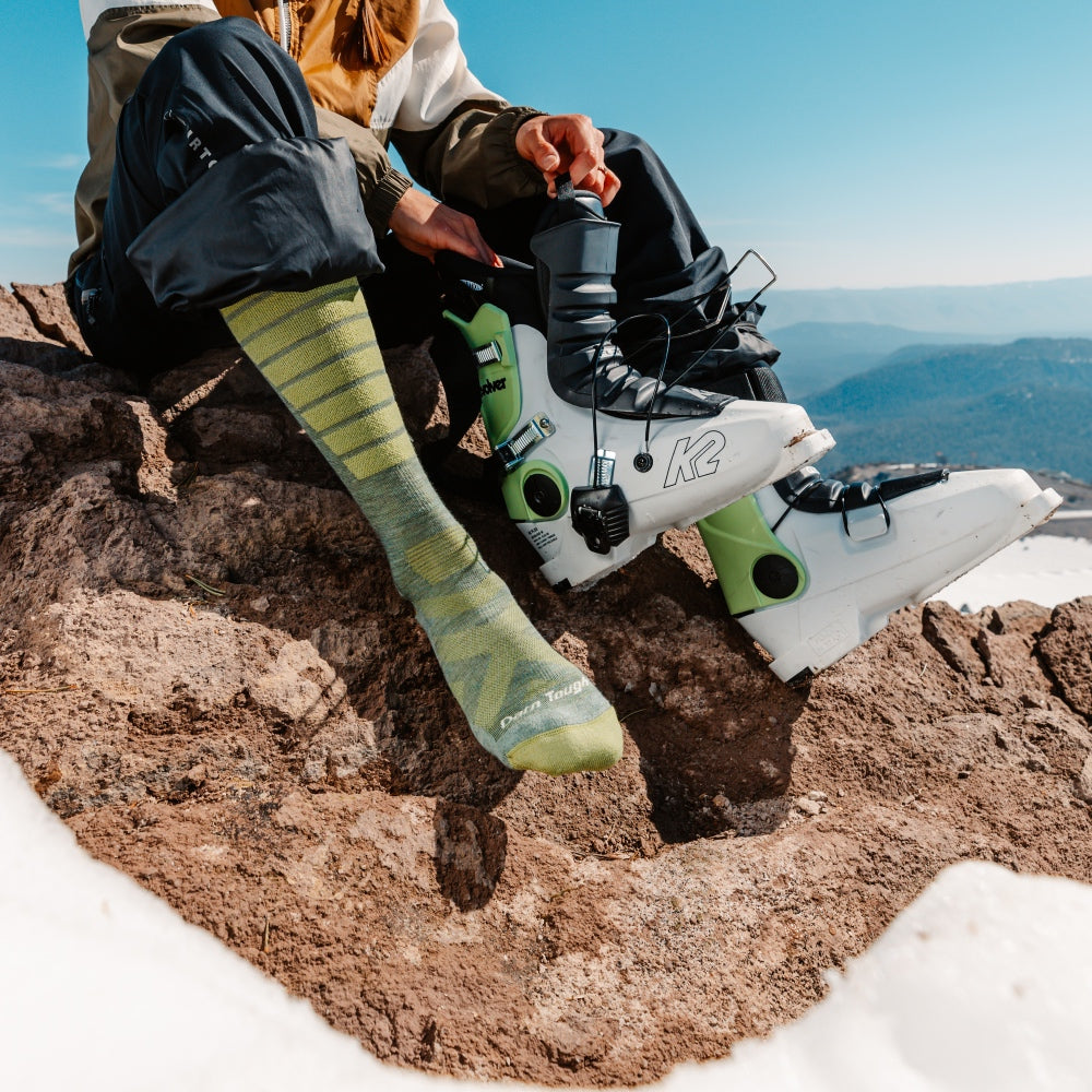 A skier on a mountain putting on their boots over merino wool ski socks