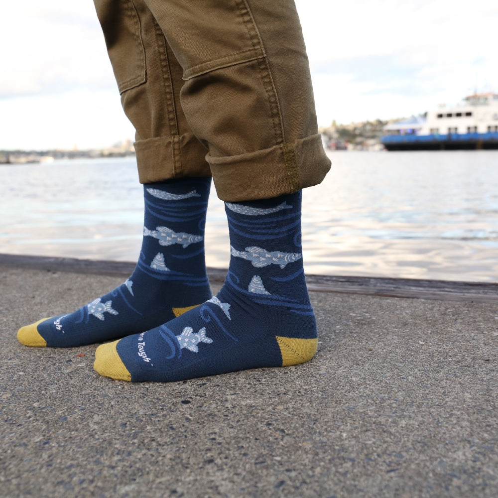 A person standing by the water wearing blue socks with alaskan salmon covering them