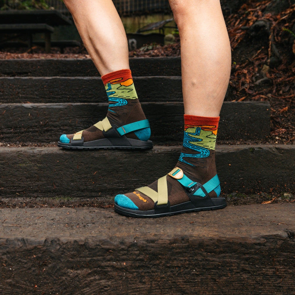 Feet standing on steps wearing Darn Tough hiking socks and sandals that show them off