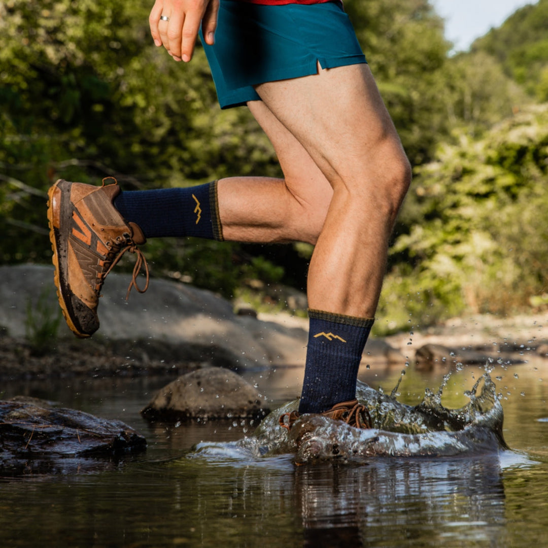 Hiker walking across a stream wearing boot hiking socks splashing water. 