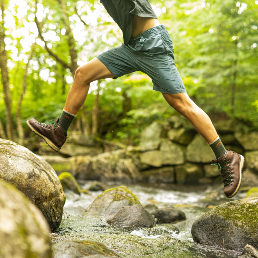 Hiker hopping in mid air from one rock to another while crossing a stream.