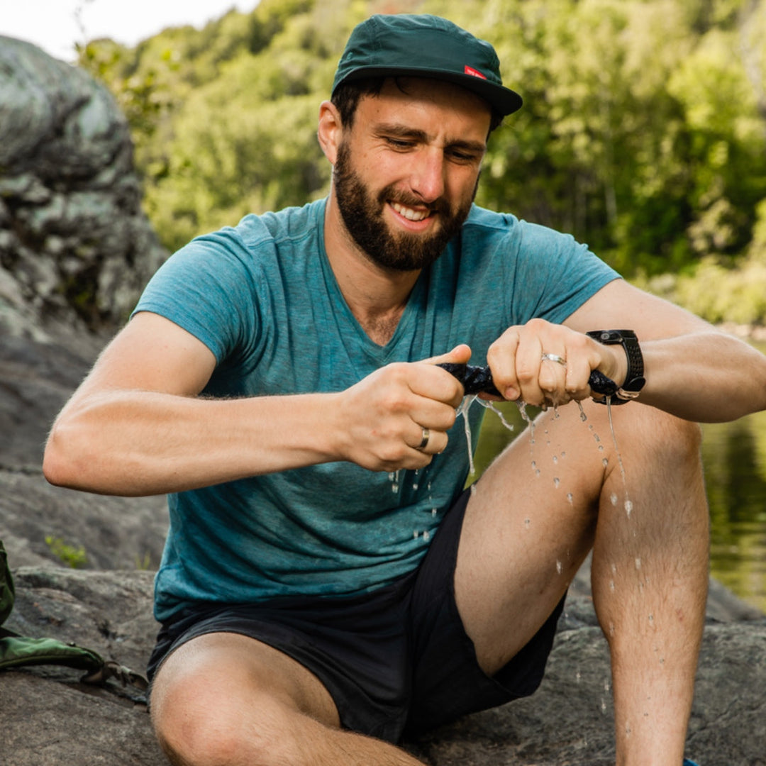 Hiker squeezing water out of their wet hiking socks while sitting on a rock.