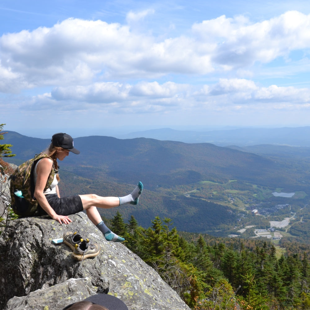A hiker with their boots of showing their Darn Tough socks with Vermont's Green Mountains behind