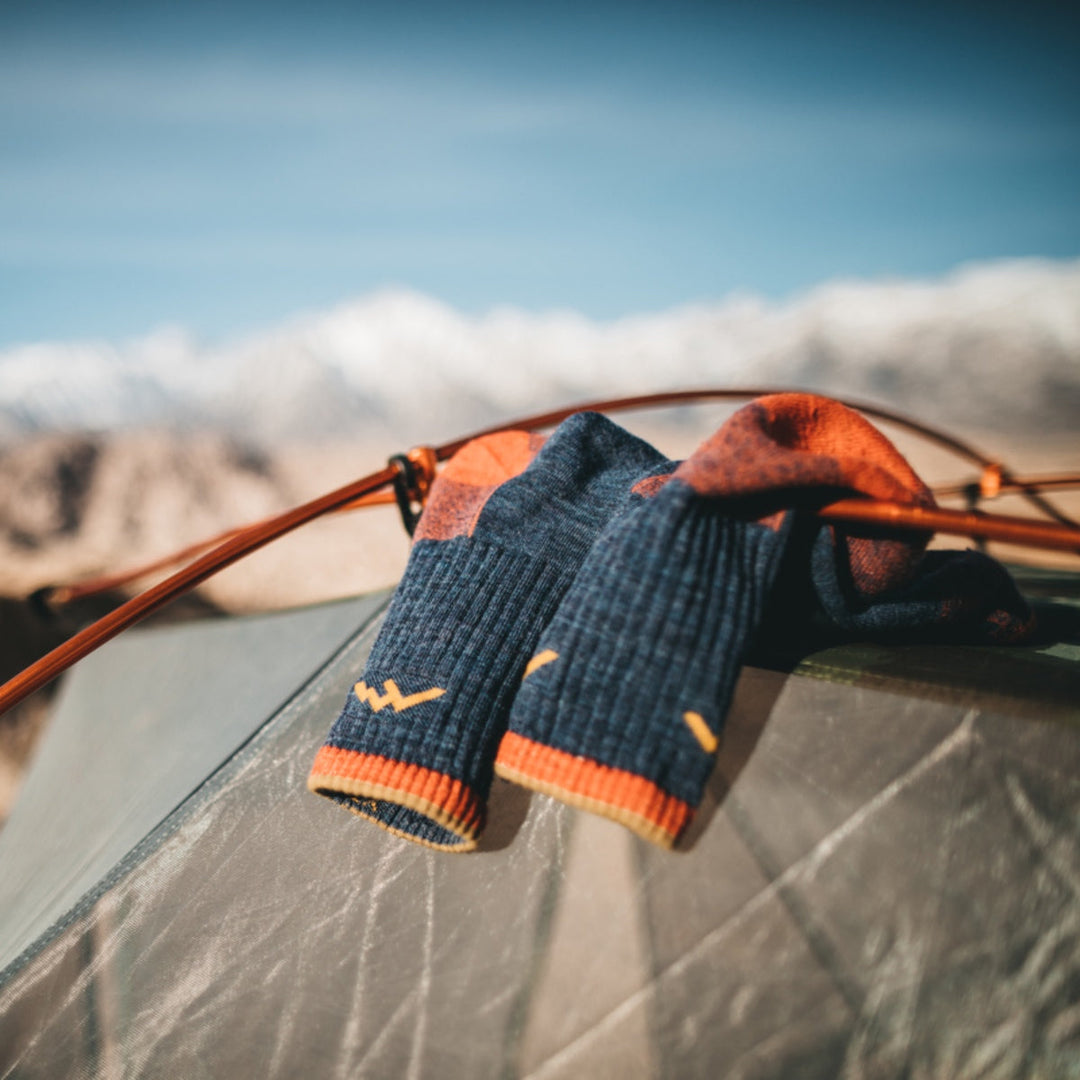 Pair of Darn Tough hiking socks resting atop a tent with mountain views in the background.