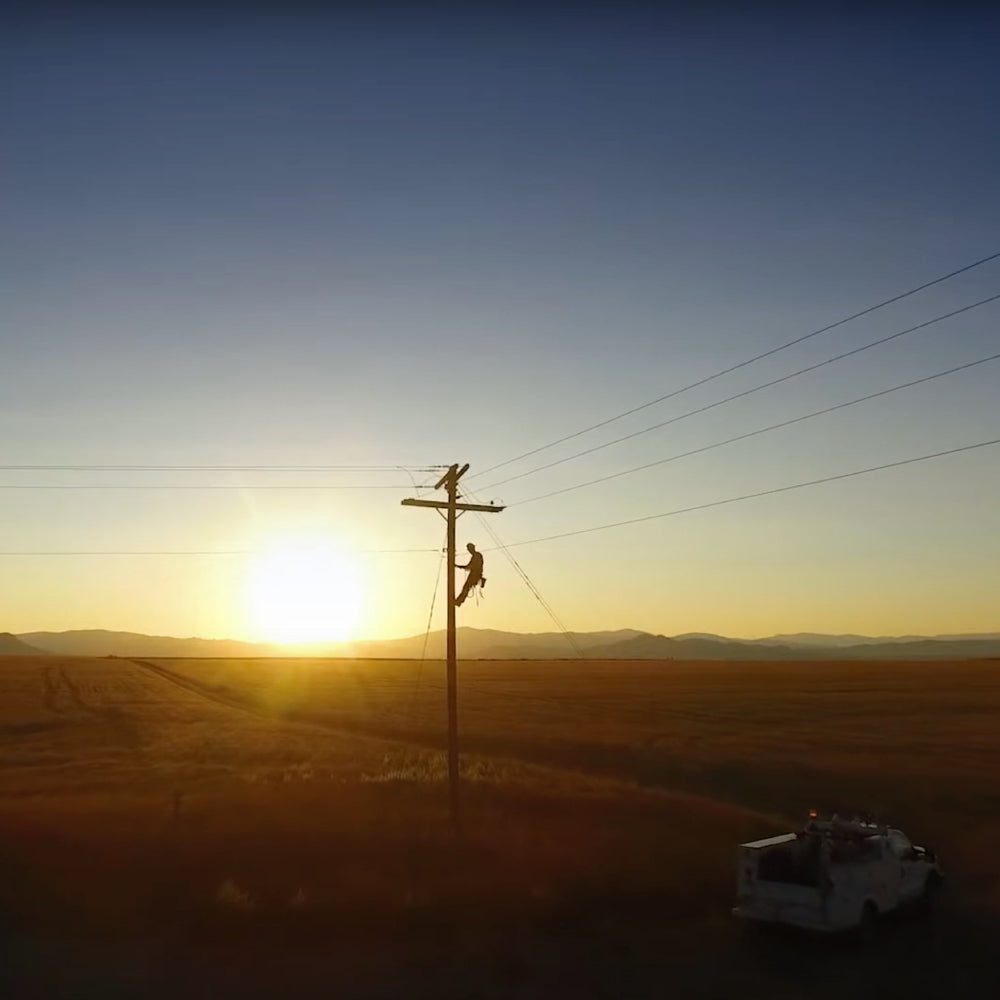 Telephone lineman high up on a pole with the sun rising behind him