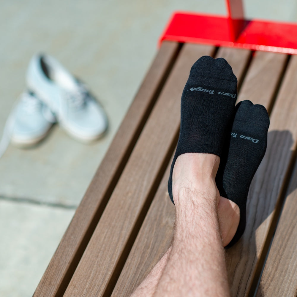 Feet wearing black men's no show dress socks, with the shoes kicked off nearby