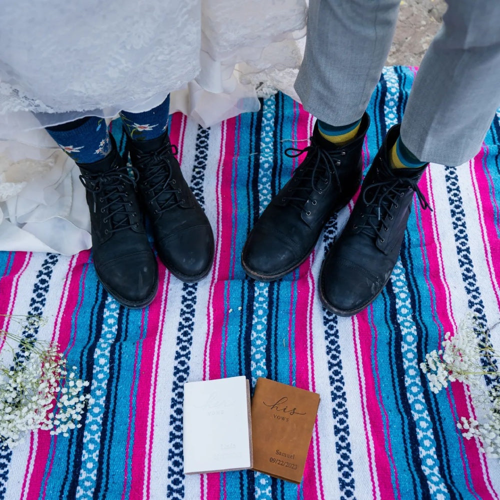 Two pairs of feet at a wedding lifting their hems to show darn tough socks