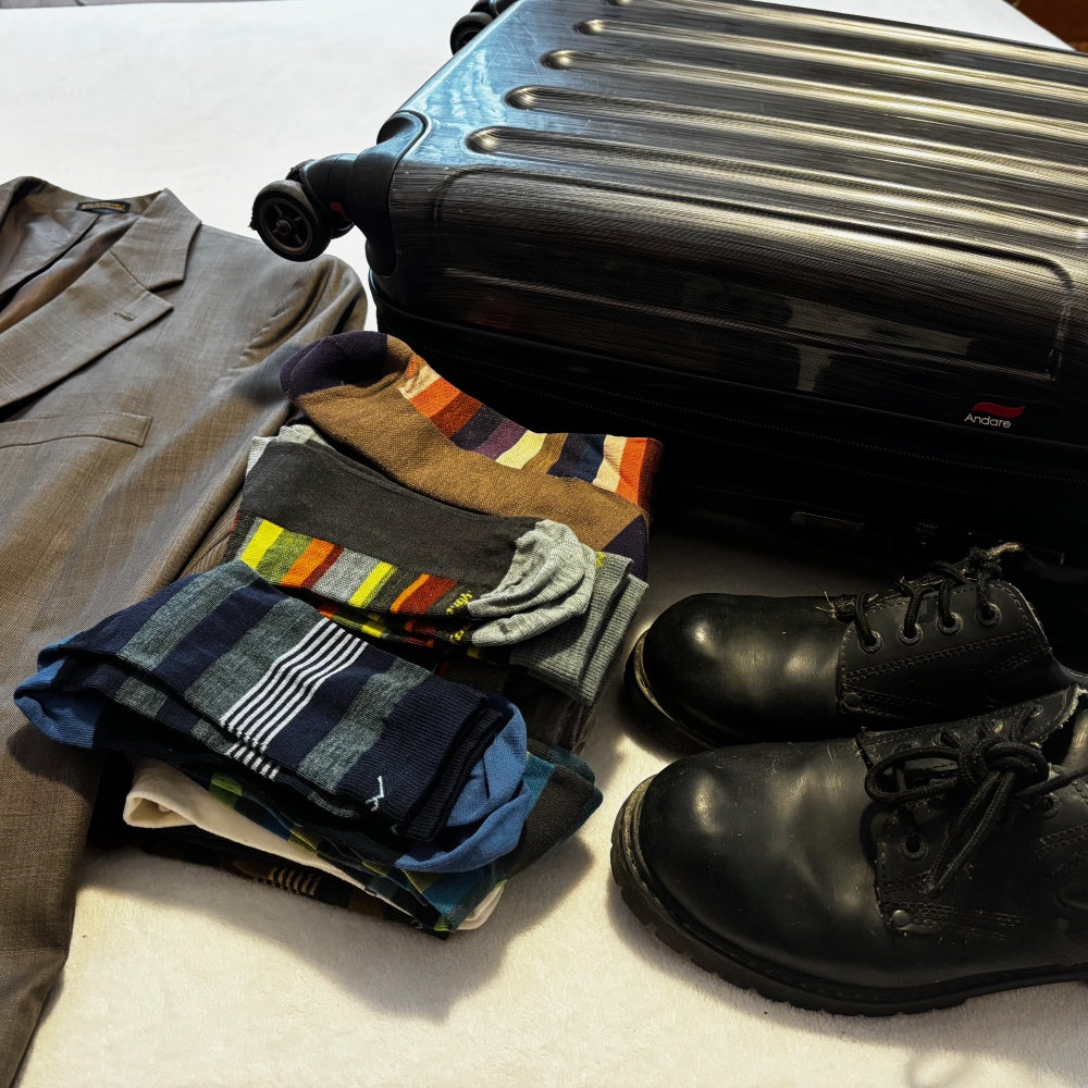 A suitcase, dress shoes, suit jacket, and dress socks all ready to pack