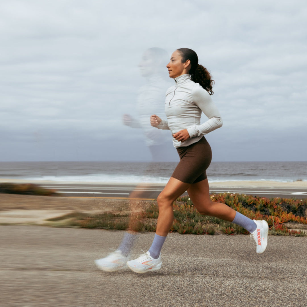 Runner running along the coast on a road wearing running socks and sneakers with motion blur.