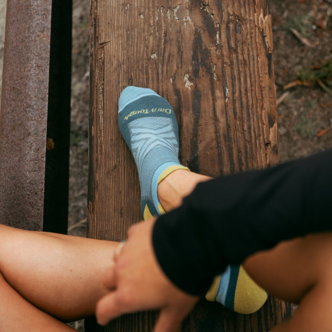 Person wearing no show running socks sitting cross-legged on a wooden bench.