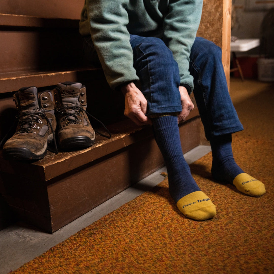 Person sitting down on steps bending over to pull up thier work socks with boots resting beside them.