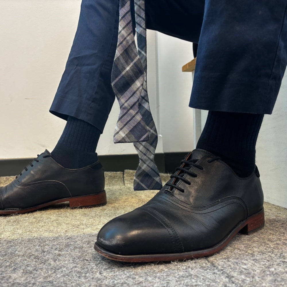 Feet wearing the best men's dress socks, shoes, slacks, and a bowtie nearby