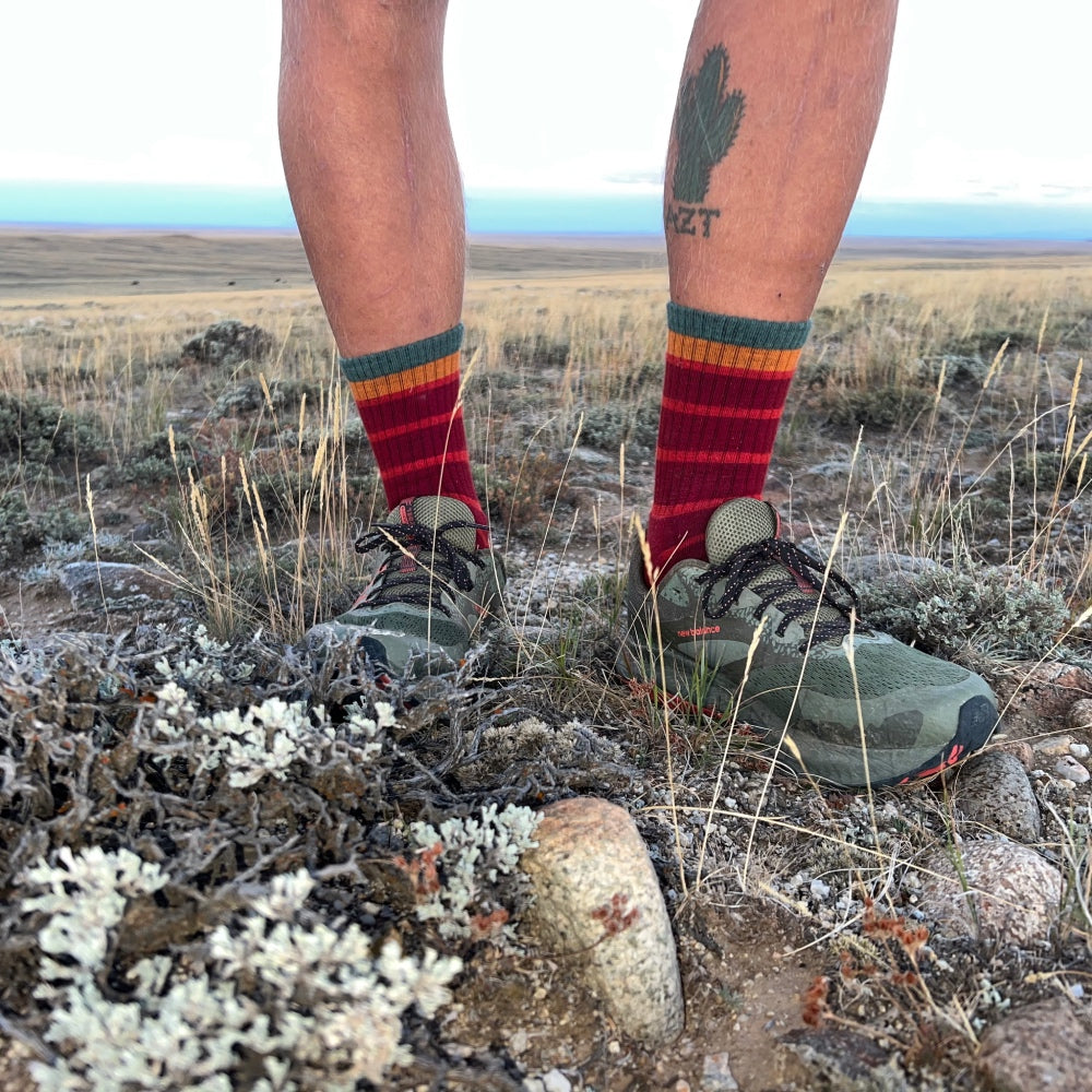 A pair of feet on the CDT wearing red Darn Tough hiking socks with stripes