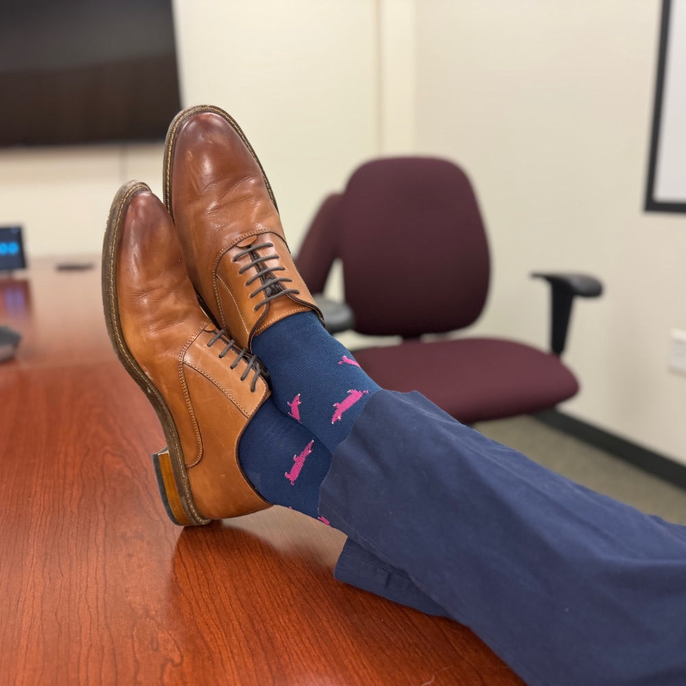 Feet up on a conference room table wearing navy blue dress socks and brown oxfords