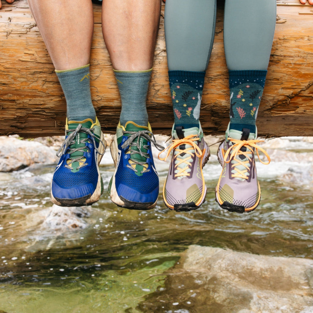 Two people sitting on a log above a stream wearing hiking socks