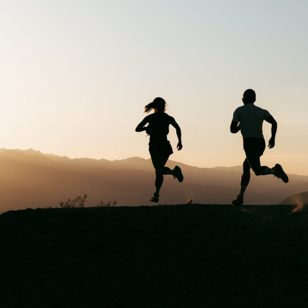 Two silhouettes running at sunset with mountains in the background.