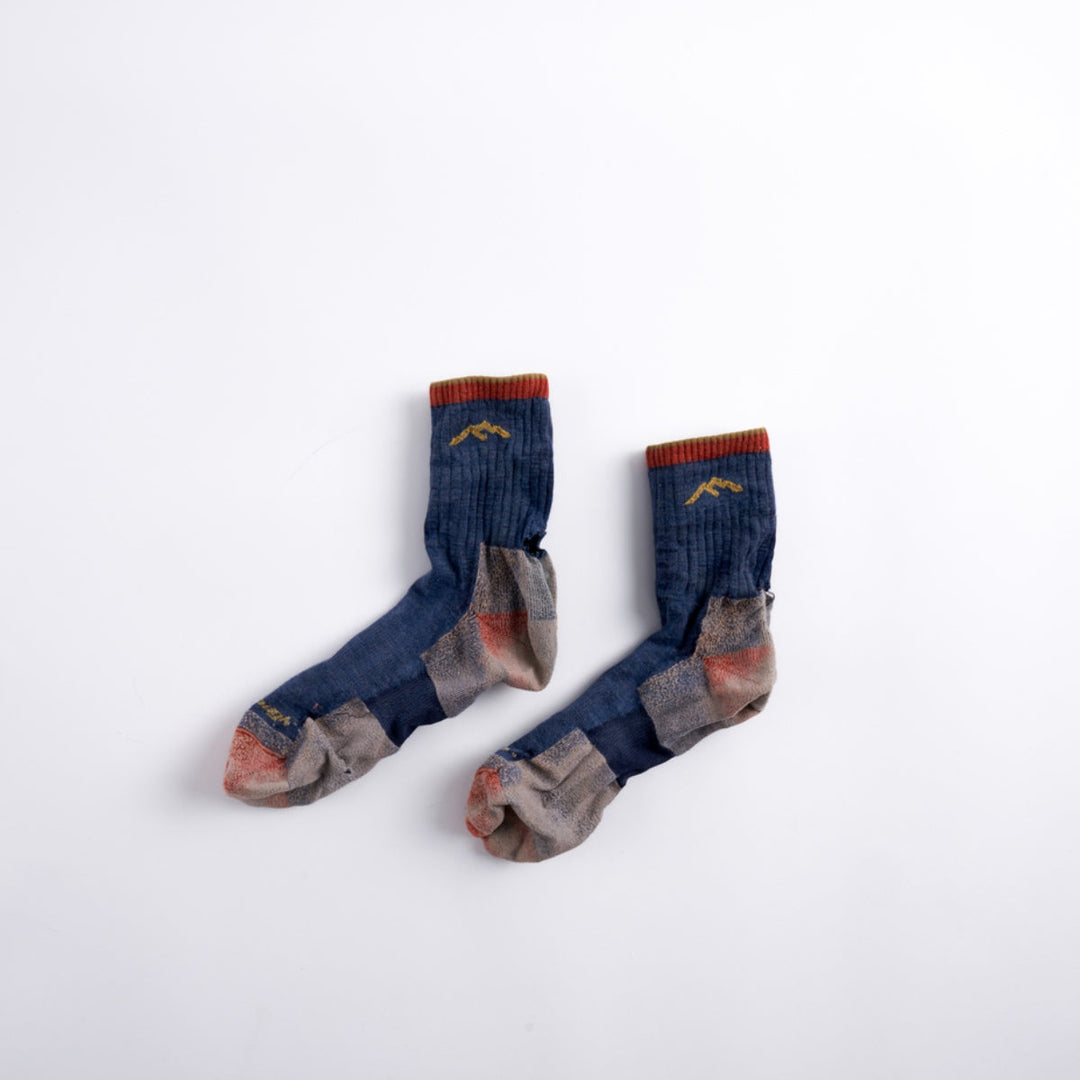 Pair of worn out darn tough socks from warranty laying flat with white background.