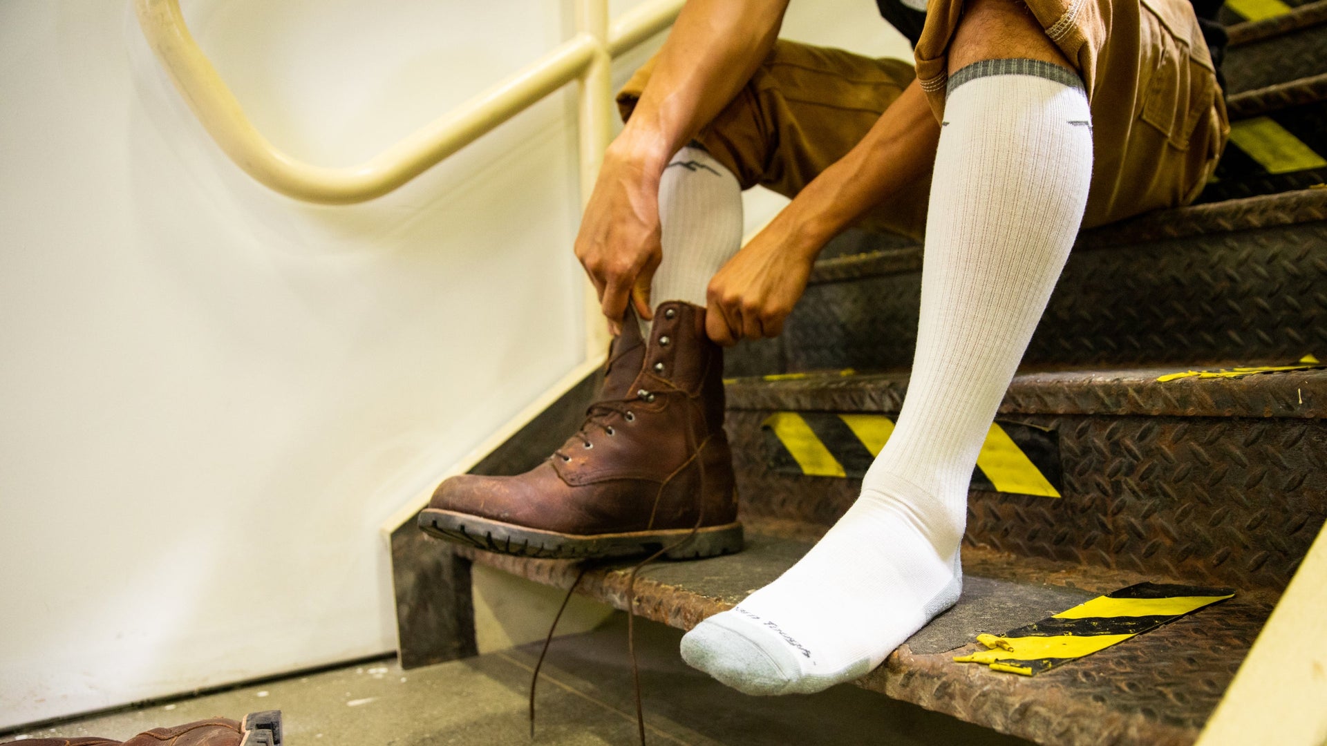 Close up of model putting on work boots wearing the Men's Westerner over the calf lightweight work sock