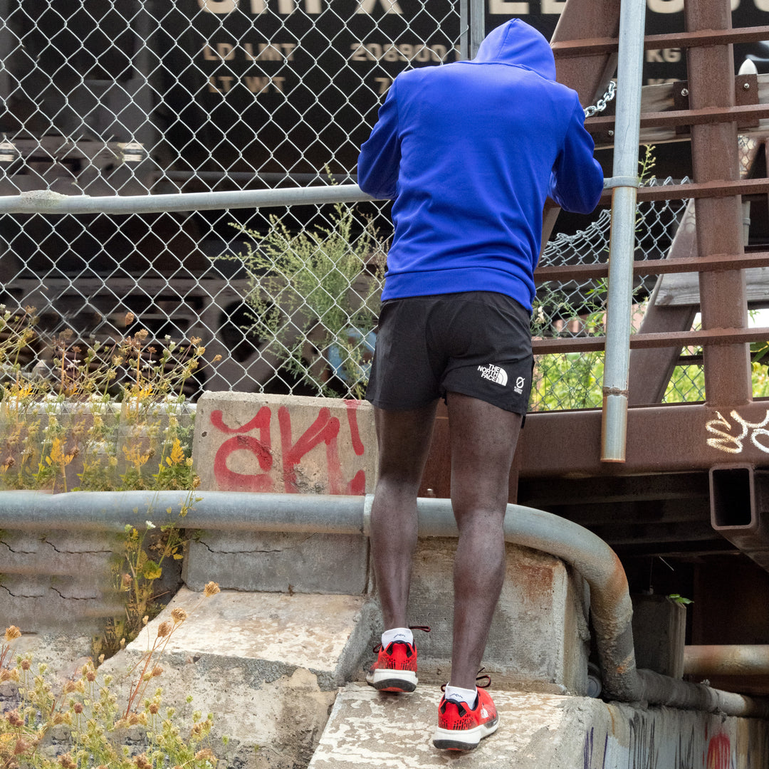 Runner leaning against a chain link fence, stretching, wearing Men's Run No Show Running socks in White