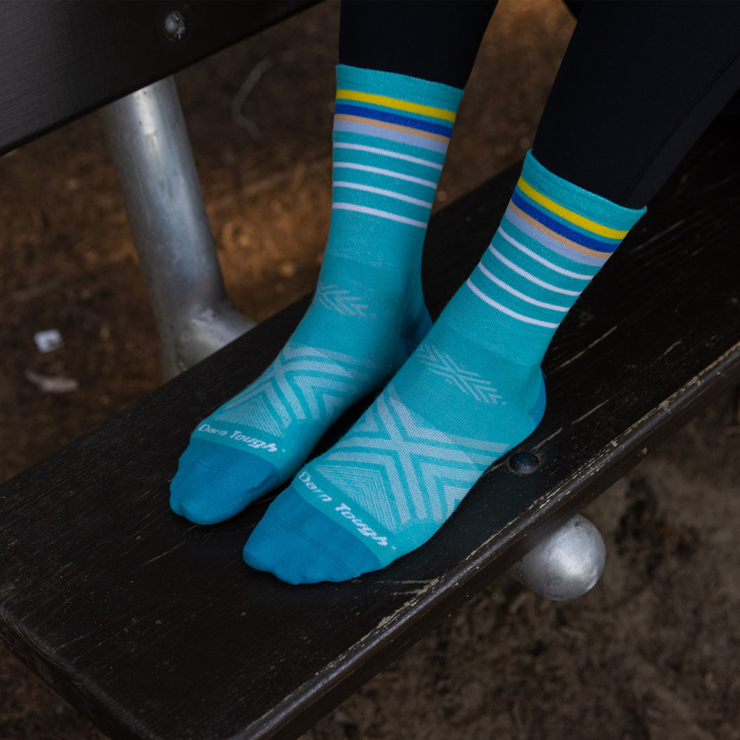 Close up shot of model sitting with her feet up on a bench wearing the women's stride micro crew running sock in teal