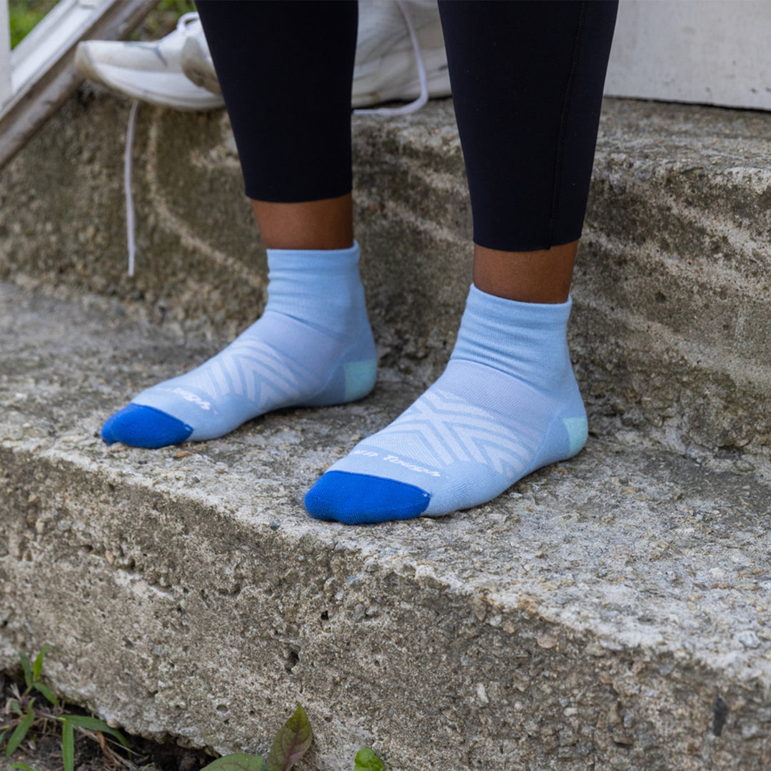 Close up shot of model standing on steps wearing the women's quarter running sock in sky blue with no shoes on