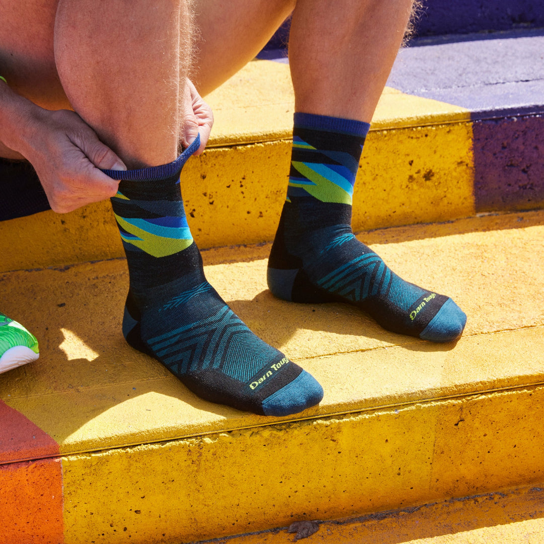 Close up shot of model sitting on colorfully painted concrete steps and pulling up 1056 socks in Black without shoes on