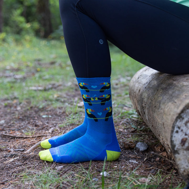 Side shot of model sitting on a log wearing the women's toco loco micro crew running sock in baltic blue