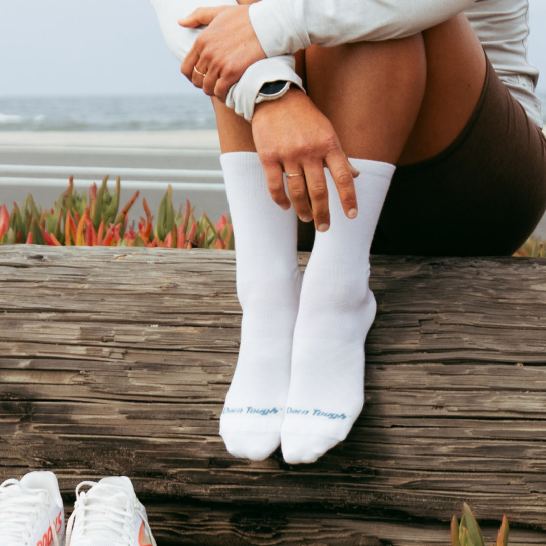 Model sitting on log next to water wearing the 1068 micro crew running sock in white colorway