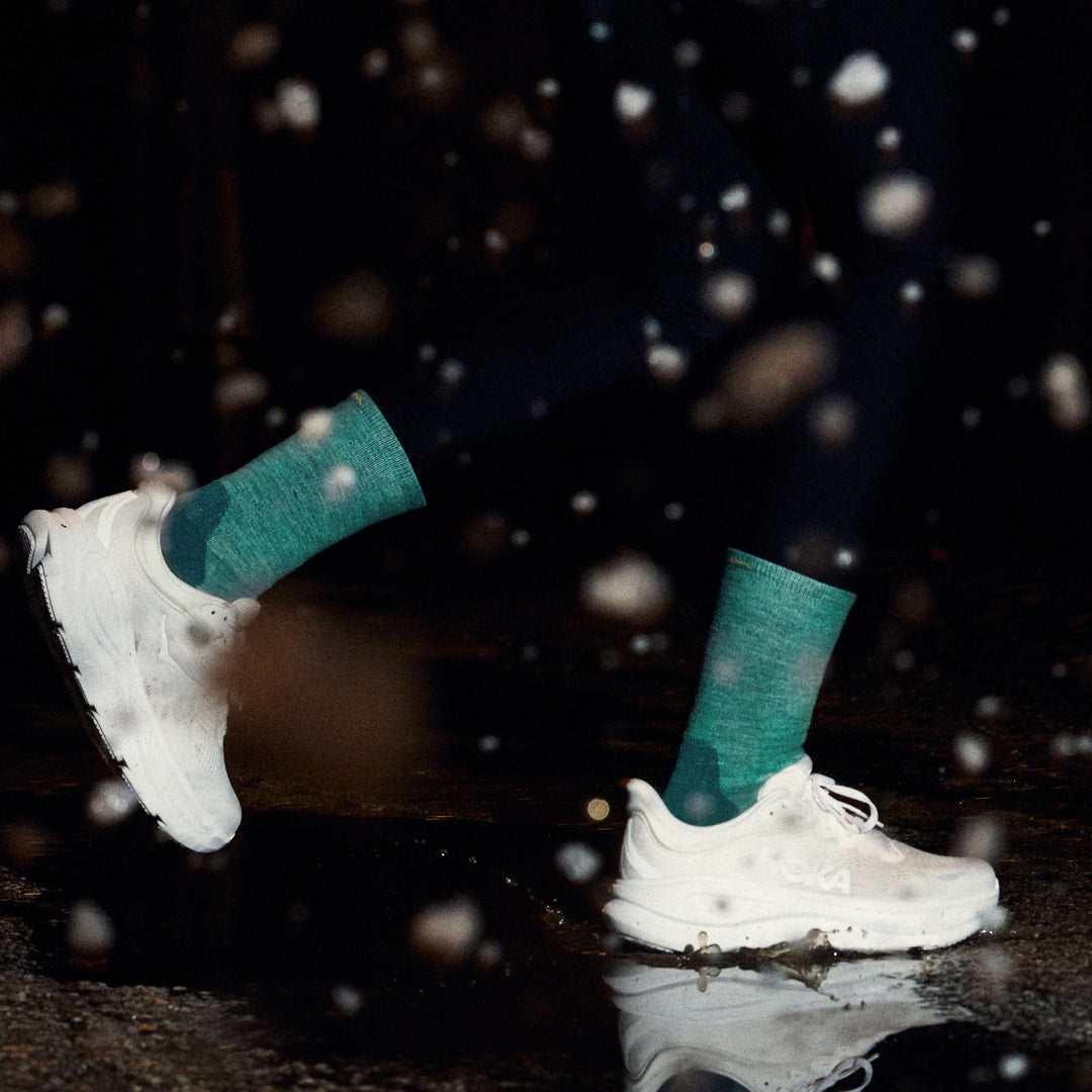 close up image of model running in dark through rain wearing white shoes and 1072 run micro crew ultra lightweight with cushion teal sock