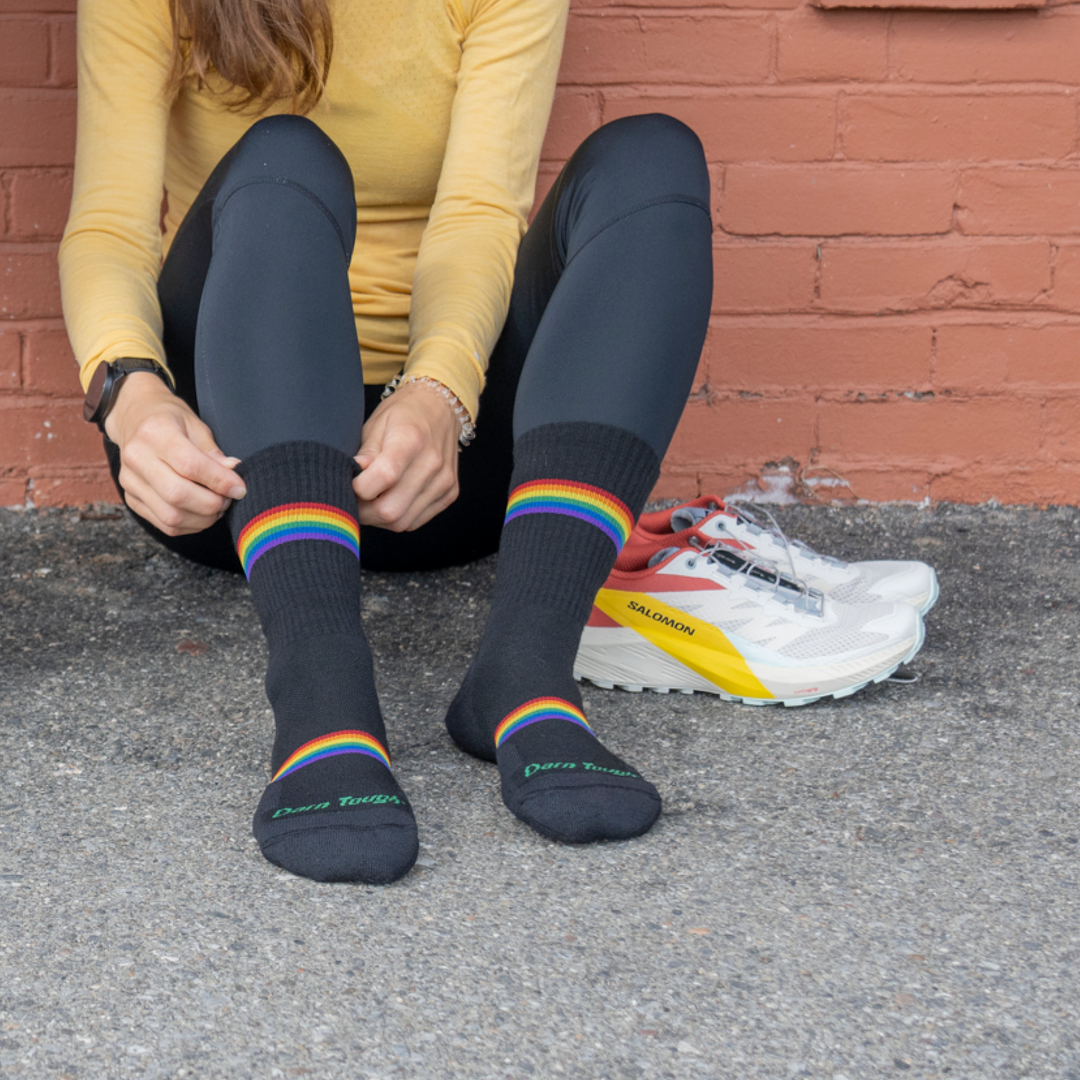 Shot of model wearing 1115 Prism Micro Crew Running socks and sitting against brick wall while adjusting cuff of the right sock.