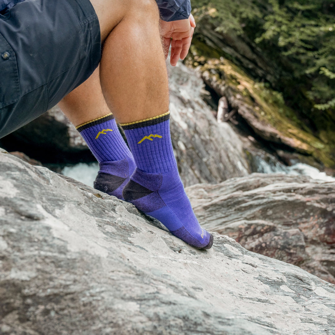 Model sitting on rocks near the water wearing the 1466 Micro crew hiking sock in ultraviolet