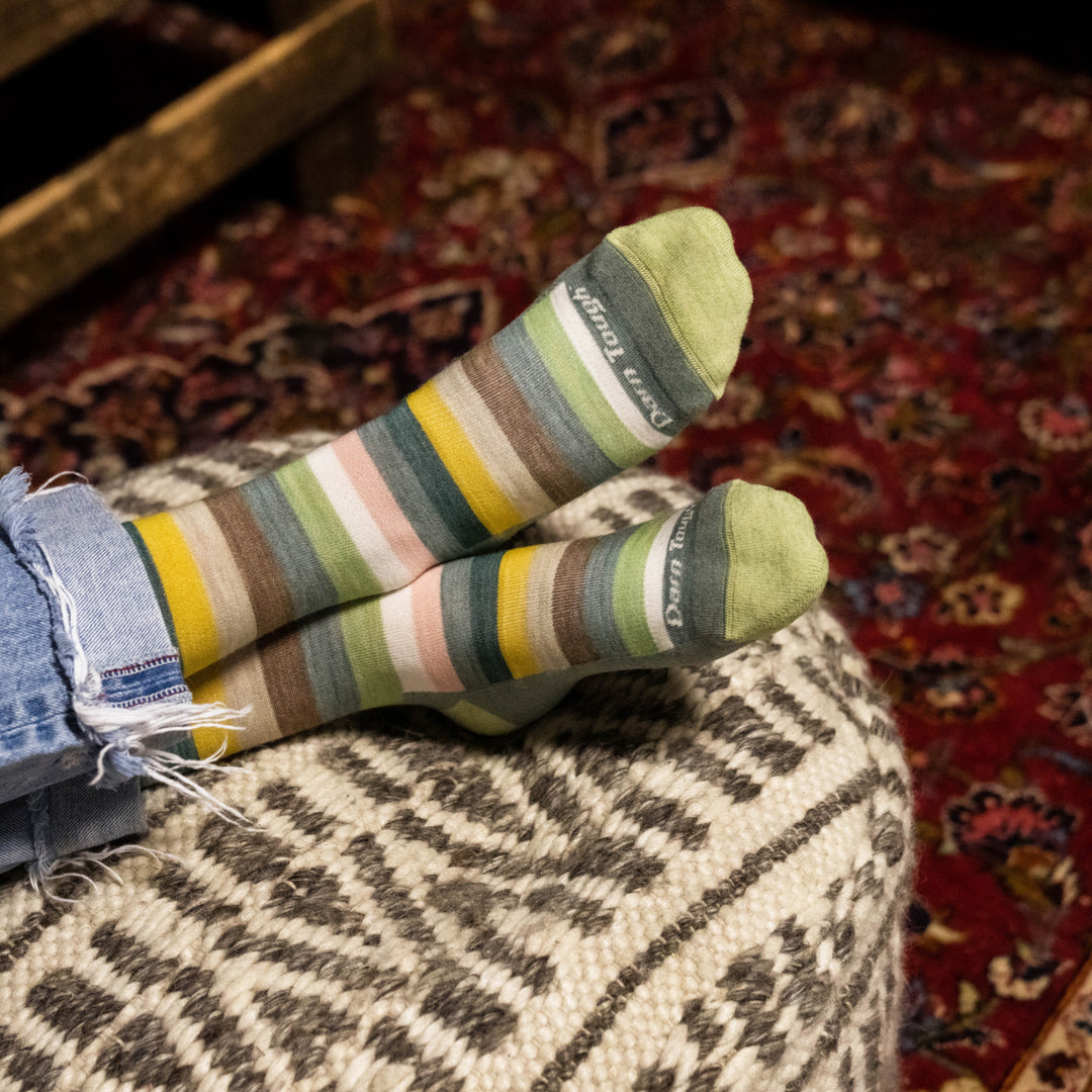 Woman resting feet on ottoman with Women's Mystic Stripe Crew sock in seafoam and wearing rolled jeans