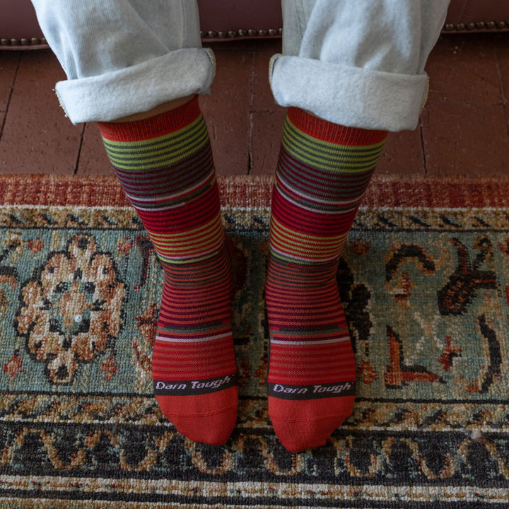 Close up overhead shot of model wearing women's pixie crew lifestyle sock in tomato red with patterned rug in background