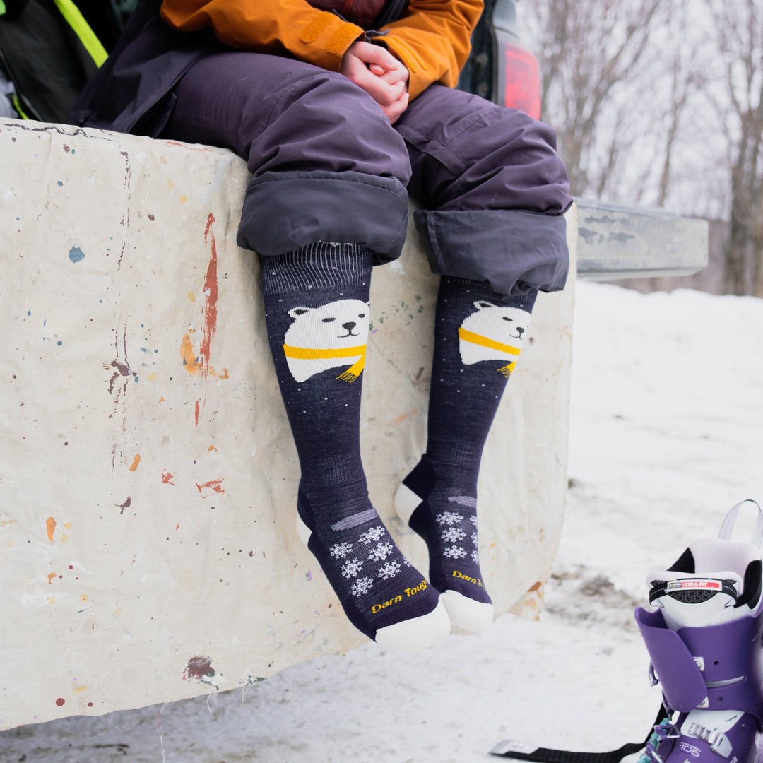 Woman wearing snowpants rolled up to the knee with Mama Bear Over the Calf Midweight Ski & Snowboard Socks in Blue